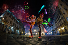 Night Street Circus Performance Whit Clown, Juggler. Festival City Background. Fireworks And Celebration Atmosphere.