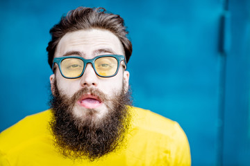 Wall Mural - Close-up portrait of a confused bearded man in yellow sweater and sunglasses on the blue background