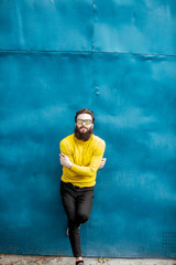 Wall Mural - Portrait of a stylish bearded man in yellow sweater posing on the blue metal wall background