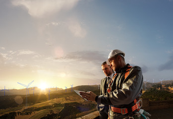 Wall Mural - Windmill engineer and businessman planing new ecology project. they standing and looking in tablet. Around wind generators blueprint and beautiful landscape