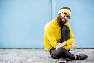 Wall Mural - Portrait of a stylish man in yellow sweater sitting on the blue wall background outdoors