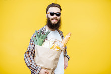 Portrait Of A Bearded Man Standing With Shopping Paper Bag Full Of Food On The Bright Yellow Background