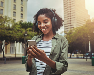 Wall Mural - Young woman using mobile phone while listening with headphones on her head