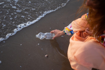 A woman cleaning a beach full of plastic bottles and rubbish in the sea