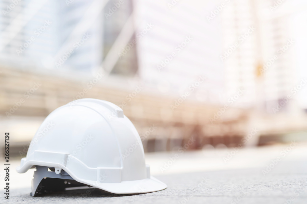 white hard safety wear helmet hat in the project at construction site building on concrete floor on city with sunlight. helmet for workman as engineer or worker. concept safety first.  - obrazy, fototapety, plakaty 