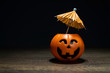 Orange Pumpkin Halloween with umbrella on wooden table in black background