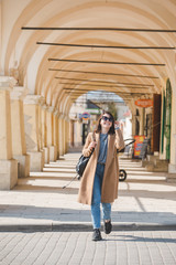 Wall Mural - young pretty fashionable woman walking in brown coat by street