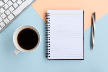 Directly above view of simple office desk with computer keyboard, pen and cup of coffee on dual tones background