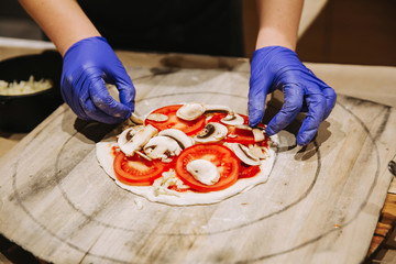 Making pizza, putting ingredients on pizza. Hands with gloves.