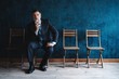 © opolja - Waiting for interview. Confident mature businessman sitting on chair against dark blue background.