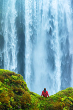 Man Sitting On A Mossy Rock At Base Of Skogafoss Waterfall; Iceland