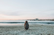 © Designpics - A girl crouches on the beach looking out over the ocean to the horizon at sunset; Long Beach, California, United States of America