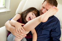 Father Tickling Daughter On Chair At Home