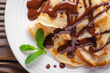 Flat lay French crepes with chocolate sauce in ceramic dish on wooden kitchen table