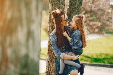 young and stylish mother with long hair and a jeans jacket playing with her little cute daughter in the summer park