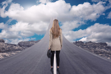 A businesswoman standing on road that goes up to the sky