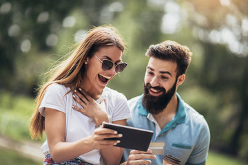 Happy couple paying on line with credit card and digital tablet outdoor