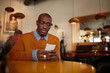 © Seventyfour - Warm toned portrait of contemporary African man using smartphone  sitting at table in cafe, copy space