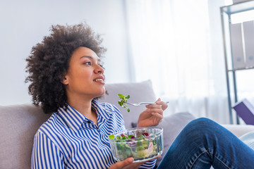 Wall Mural - Happy woman relaxing on the sofa eating salad in her living room