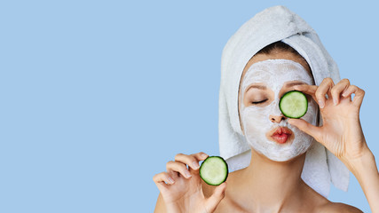 beautiful young woman with facial mask on her face holding slices of cucumber. skin care and treatme