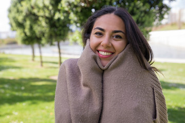 Smiling woman wrapping up in cardigan in city park