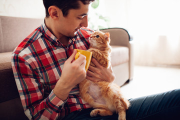 Young man holding a cat and drinking tea at home