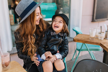 Portrait happy loving family, mother and doughter sitting in city cafe playing and hugging. Mother and daughter laugh sincerely. Styling family, true emotions, good day.