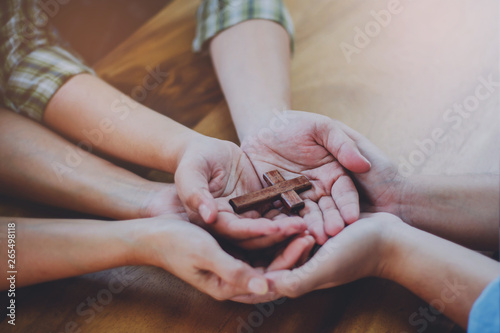 Three people hands holding small wooden cross on wood table, Christian concept Jesus is the center of life or ministry , copy space.