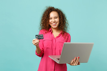 Wall Mural - Cheerful african girl in casual clothes using laptop pc computer, hold credit bank card isolated on blue turquoise background in studio. People sincere emotions lifestyle concept. Mock up copy space.