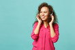 © ViDi Studio - Charming african girl in casual clothes looking aside, listening music with headphones isolated on blue turquoise background in studio. People sincere emotions, lifestyle concept. Mock up copy space.