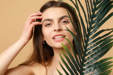 Wall Mural - Close up brunette half naked woman 20s with perfect skin, nude make up palm leaf isolated on beige pastel wall background, studio portrait. Health care cosmetic procedures concept. Mock up copy space.