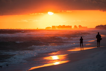 Young Couple Watching Dramatic Orange Red Sunset In Santa Rosa Beach, Florida With Pensacola Coastline Coast Skyline In Panhandle With Ocean Gulf Of Mexico Waves
