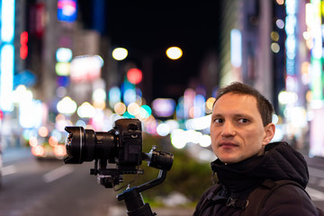 Tokyo, Japan Shinjuku district at night with young man portrait photographer videographer filming with camera and gimbal with background of bokeh lights on street