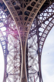 Fototapeta Paryż - Eifel Tower column bottom up low angle shot from tower basement with blue sky background and violet sun light poke through metal grid 
