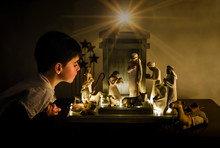 Young Boy Leaning In Looking Closely At A Ceramic Nativity Scene.