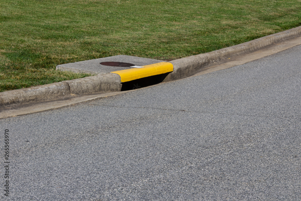 Residential street curb with drain painted yellow, green grass and ...