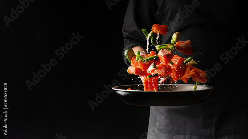 Cuadros en Lienzo Chef prepares pieces of salmon or trout fillet with green beans in a pan, on a b