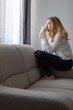 © bonciutoma - Caucasian blonde woman sitting on a sofa drinking her morning coffee in front of a window, casual and relaxed