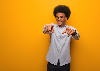 Wall Mural - Young african american man over an orange wall cheerful and smiling pointing to front