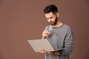 Thoughtful male programmer with laptop on color background