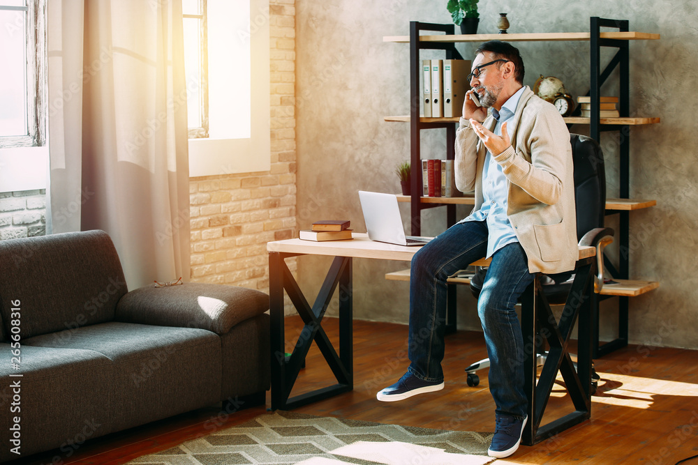 Handsome mature man talking by mobile phone at home