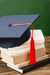 Poster - books and academic cap on wooden surface isolated on green