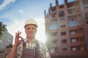 Senior engineer smiling broadly showing up gesture ok to camera, expression of like and approval. Sunset time