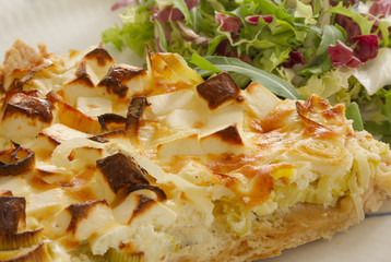 A slice of quiche with leek and feta or goats cheese on a plate with crispy leaf green salad. Vegetarian food in close up image.