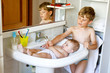 © Irina Schmidt - Cute adorable baby taking bath in washing sink and grab water tap.