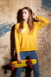 © Kiryl Lis - Portrait of positive young attractive girl wearing yellow blouse and blue jeans holding yellow skateboard.