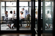 © Monkey Business - Middle aged white businessman stands addressing colleagues at meeting, seen through glass wall