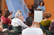 © Monkey Business - Woman At Podium Chairing Neighborhood Meeting In Community Centre