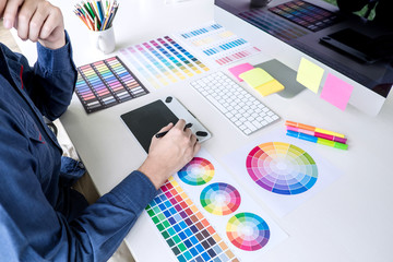 Poster - Male creative graphic designer working on color selection and color swatches, drawing on graphics tablet at workplace with work tools and accessories