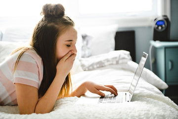 Wall Mural - A Young smiling teen girl on bed with laptop